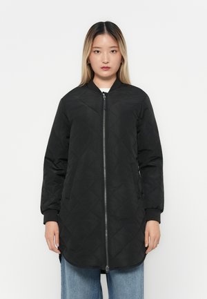 Manteau long matelassé noir avec fermeture éclair, poignets côtelés et poches latérales. Présente un col rond et un ourlet droit.