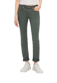 Pantalones verdes de mezcla de algodón con un corte ajustado, puños enrollados y bolsillos frontales, combinados con zapatillas blancas y una camiseta blanca ajustada.