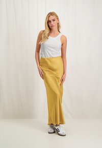 Geel satijnen maxi rok gecombineerd met een witte geribbelde tanktop en witte sneakers met zwarte accenten; gladde textuur, getailleerde silhoeet.