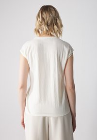 Jasnokremowy top z krótkim rękawem. Miękki, lekki materiał o gładkiej fakturze. Prosty krój z zaokrąglonym dekoltem i luźnym fasonem.