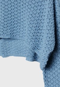 Tissu tricoté bleu clair avec un motif texturé, présentant un tissage doux et lâche ainsi que des bords effrangés.