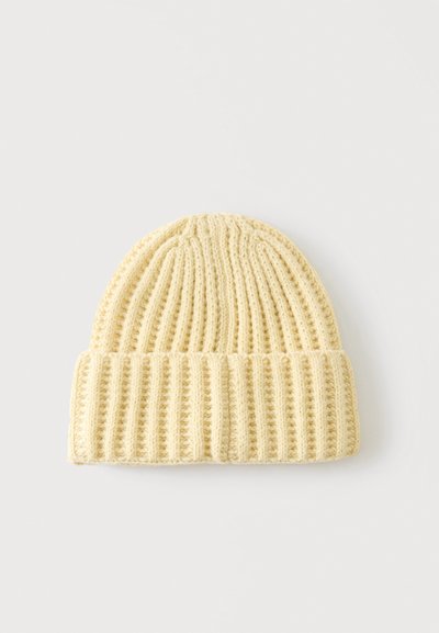 Bonnet en maille côtelée de couleur crème avec un revers, présenté sur un fond uni gris clair.