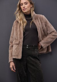 Umělá koženka v světle béžové barvě, s předním zipem a bočními kapsami, kombinovaná s tmavými kordovými kalhotami s dvojitým zapínáním.