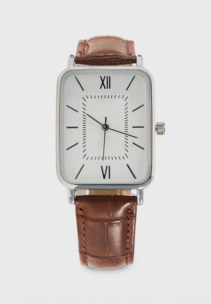 Montre carrée en argent avec cadran blanc, chiffres romains noirs et marqueurs, aiguilles noires et bracelet en cuir marron avec surpiqûres.
