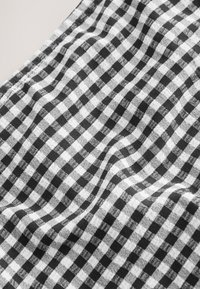 Material alb-negru în carouri cu un model clasic gingham, cu o suprafață moale, texturată și ușor ridată pe toată suprafața.