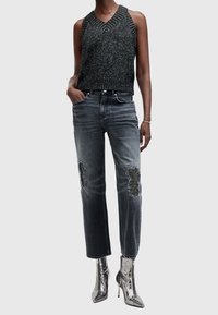 Svart och silverfärgad stickad ärmlös topp, grå denimjeans med pärlbroderade lappar på knäna och metaliska ankelboots med spetsig tå.