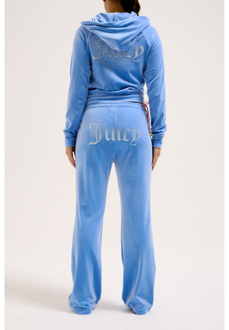 Blauwe velours trainingspak met capuchon. Kenmerkt zich door "Juicy" in rhinestones op de achterkant en de broek. Met een trekkoord in de taille en een ontspannen pasvorm.