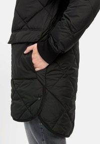 Schwarze gesteppte Pufferjacke mit einer Seitentasche, strukturierten Ärmeln und abgerundetem Saum. Das Material ist glatt und leicht.