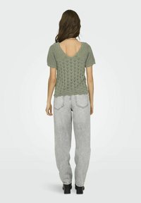 Top de punto verde de manga corta con escote en V, combinado con unos jeans baggy grises de talle alto y unas botas negras de suela gruesa.