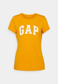 Camiseta de algodón amarilla con un logo blanco de "GAP" en forma de arco. Cuello redondo clásico y mangas cortas con un ajuste regular.