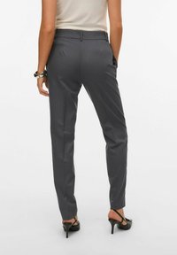 Grå skreddersydde bukser med rett ben, hakke-midje og to baklommer. Jevn tekstur og subtil glans, kombinert med sorte høyhælede sko.