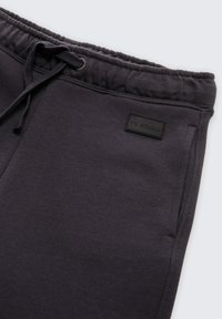 Dunkelgraue Sweatpants aus weichem Material, mit einem elastischen Bund und Kordelzug, Seitentaschen und einem kleinen schwarzen Logo-Patch.
