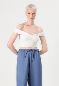 Bela crop majica brez naramnic z volančki, v kombinaciji z ohlapnimi modrimi hlačami na vrvico iz lahkotnega materiala.