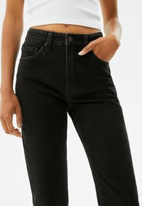 Jeans de mezclilla negros de cintura alta con una textura suave, diseño de cinco bolsillos y un cierre de botón metálico en la cinturilla.