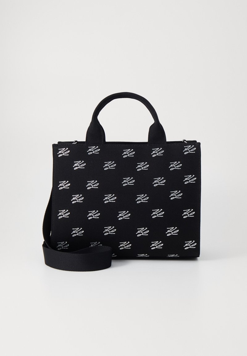 Černá textilní taška s bílým opakujícím se vzorem loga, vybavená dvěma krátkými uchy a odnímatelným ramenním popruhem. Obdélníkový tvar, zapínání na zip.