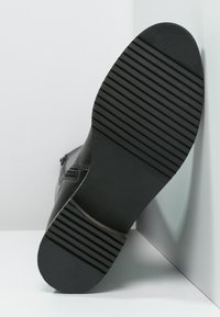 Bottines en cuir noir avec une semelle texturée, dotées d'une fermeture éclair sur le côté et d'un bout arrondi. La semelle présente des rainures horizontales pour une meilleure adhérence.