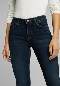 Jeans skinny azul oscuro con cintura alta, que presentan costuras naranjas en contraste, un botón de metal y diseño clásico de cinco bolsillos.