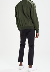 Groene bomberjack met elastische manchetten en onderkant, gecombineerd met donker Slim-fit broeken en witte sneakers, gezien van de achterkant.