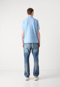 Himmelblå polo-skjorte med klassisk krage, kombinert med falmede blå jeans. Jeansene har baklommer med et subtilt design.