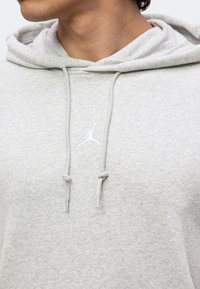 Gros plan d'une personne portant un sweat à capuche gris clair avec des cordons et un petit logo blanc Jumpman sur la poitrine.