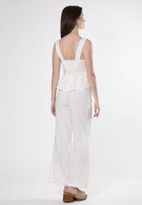 Top bianco a peplum con spalline larghe, schiena testurizzata, abbinato a pantaloni bianchi larghi e scarpe con plateau beige. Tessuto morbido e leggero.
