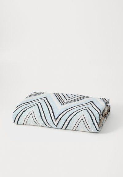 Multicolored blanket featuring a zigzag pattern in blue, black, and white tones; soft texture; neatly folded with visible edges.