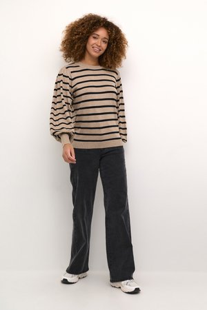 Pull beige à rayures horizontales noires, encolure ronde et manches bouffantes ; associé à un jean gris foncé évasé et des sneakers blanches.