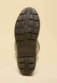 Čierna podrážka gumenej čižmy s hlbokým vzorom dezénu, ktorý obsahuje drážky a výčnelky pre lepšiu trakciu. Obsahuje vyrazený názov značky a logo.