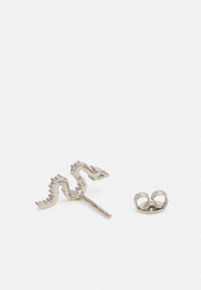 Tige de boucle d'oreille en argent en forme de zigzag ondulé avec un petit fermoir papillon séparé sur une surface blanche.