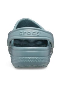Crocs i en ljusblå färg med en strukturerad yta, öppen baksida och justerbart band. Anmärkningsvärda dräneringshål på sulan.