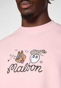 Felpa rosa con un motivo raffigurante un cane cartone animato e una pallina da golf con un cappellino a quadri, delineata da cuciture nere. Texture liscia.