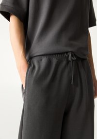 Grijze t-shirt met een relaxte pasvorm en korte mouwen, gecombineerd met bijpassende broek met trekkoord. Zacht materiaal met een gladde textuur.