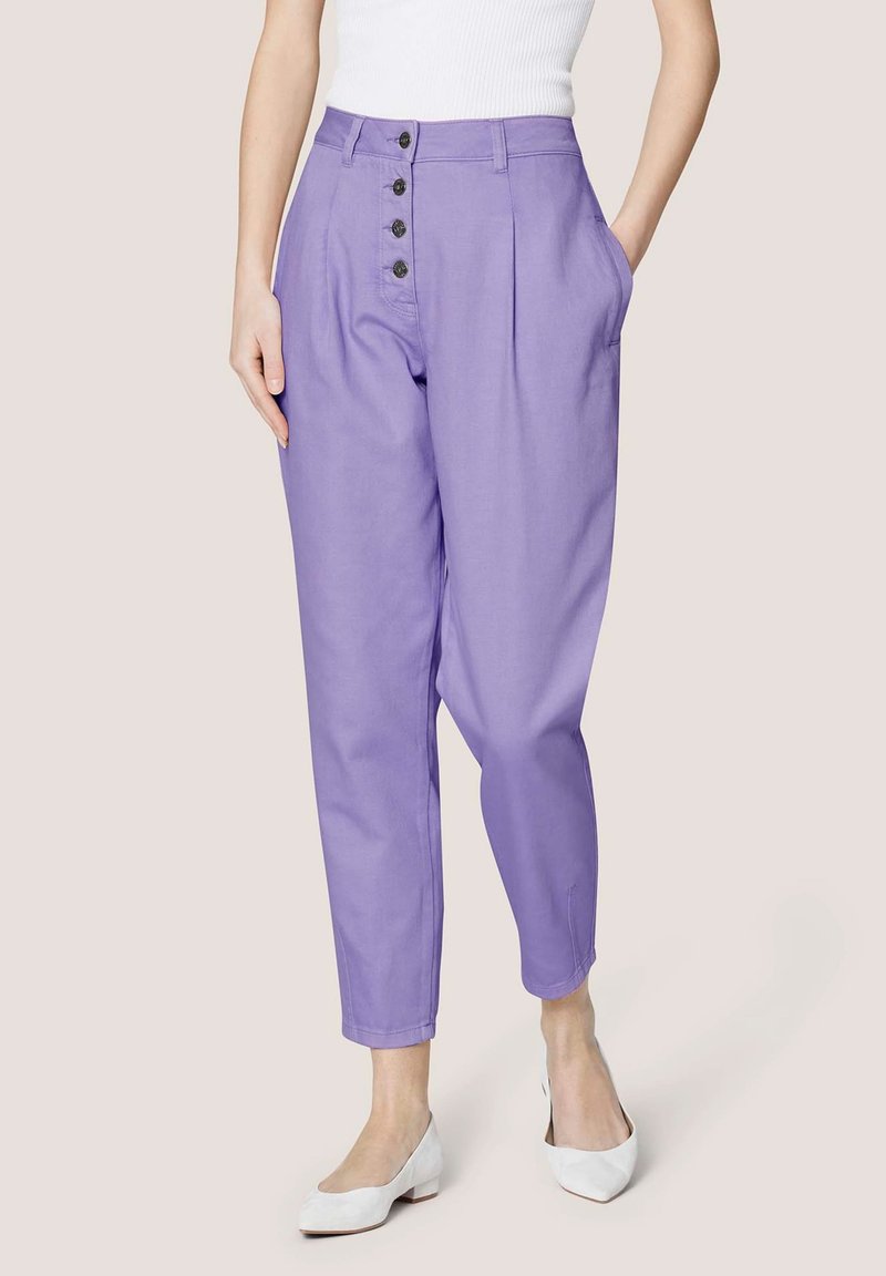 Lila, high-waisted broeken met voorplooien, sluiting met vijf knopen, zijzakken en taps toelopende pijpen. Gecombineerd met witte schoenen.