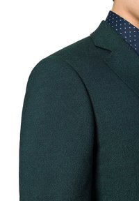 Ciemnozielona, teksturowana marynarka o dopasowanym kroju, z klapami w kształcie notched oraz subtelnym wzorem w tkaninie, dopełniona granatową koszulą.