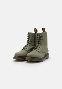 Bottines en cuir vert avec bout rond, design à lacets et coutures jaunes. Dotées d'une languette au talon pour un enfilage facile.