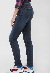 Jeans skinny de talle alto en azul oscuro con una textura suave y bolsillos traseros. Combinados con zapatillas chunky blancas, rojas y azules.