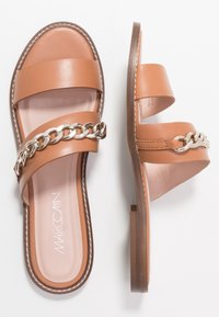Leren sandalen in bruin met twee brede banden en een zilveren kettingaccent. Platte zool met lichte demping en zichtbare stikseldetails.