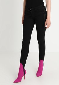 Svarta tajta jeans med hög midja, med sidodetaljer som glittrar. Matchas med klarröda spetsiga klackar. Slät textur.