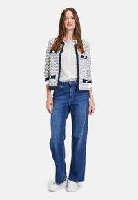 White textured jacket with navy accents, paired with blue wide-leg jeans and white sneakers. Button details on the jacket.