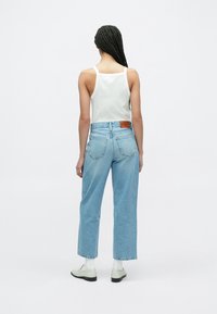 Világoskék széles szárú farmer magas derékkal és hátsó zsebekkel, fehér ujjatlan top és szürke cipők kíséretében.