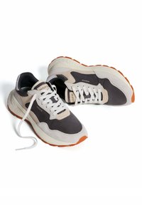 Zapatillas para hombres con una mezcla de ante gris y beige, cordones blancos, cuello acolchado y una suela de goma naranja. Nombre de la marca "HOFF" visible.