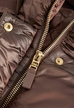 Section de veste puffy marron avec une fermeture éclair dorée, un bouton-pression doré et une texture lisse. Détails notables incluent un tissu matelassé et un tirette de fermeture éclair.