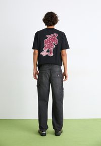T-shirt en coton noir avec un graphique de panthère rouge au dos, associé à un pantalon cargo gris foncé avec plusieurs poches.