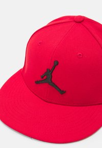 Căciulă roșie cu coada dreaptă, având pe față un logo Jumpman brodat în negru. Fabricată dintr-un material texturat.