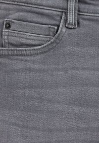 Šedá denimová tkanina zobrazující detailní záběr na kapsu, s jemnou texturou a malým černým knoflíkem.