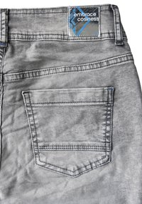 Il tessuto di denim grigio presenta una tasca posteriore con un bordo cucito. Un'etichetta rettangolare mostra "abbraccia il comfort" in blu su uno sfondo lucido.