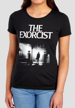 Woman wearing a black T-shirt with "THE EXORCIST" text and a silhouette of a man standing in a lit street scene at night.