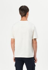 T-Shirt mit kurzen Ärmeln und Rundhalsausschnitt aus cremefarbener Baumwolle. Hat eine lockere Passform und ein schlichtes Design, mit sichtbaren Nähten entlang dem Saum und den Ärmeln.