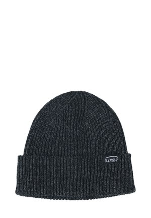 Bonnet en tricot gris foncé avec une texture côtelée épaisse. Il possède un revers repliable et une étiquette avec le logo Oxbow sur le côté.