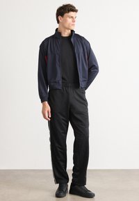 Ναυτικό μπουφάν με φερμουάρ και κόκκινες λεπτομέρειες, συνδυασμένο με μαύρο αθλητικό παντελόνι που έχει πλαϊνές ρίγες. Οι μαύρες αθλητικές σφυρίγες ολοκληρώνουν την εμφάνιση.